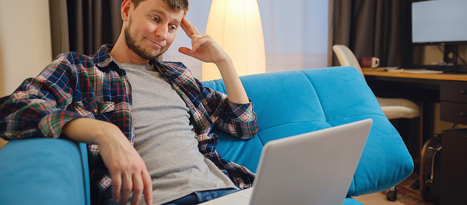 Chico joven sentado en un sofá y utilizando un ordenador portátil